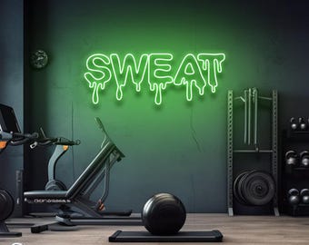 May include: Green neon sign with the word "SWEAT" dripping down in a gym setting. The sign is on a dark green wall with a black exercise bike and a black weight rack in the background.