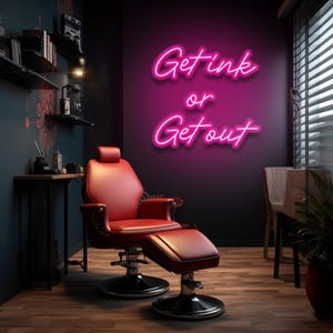 Puede incluir: Un letrero de neón rosa con el texto "Get Ink or Get Out" colgado en una pared en una habitación con una silla de barbero de cuero rojo y un reposapiés.
