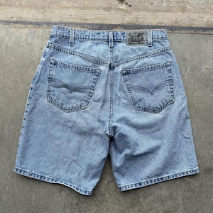 May include: Pale blue denim shorts with a classic five-pocket design. The shorts have a faded wash and a leather patch at the back waistband. The shorts have a straight leg cut and are made of durable denim.