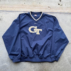 May include: Navy blue pullover windbreaker with a V-neck and gold trim. The front features a gold "GT" logo and a small Nike swoosh. The windbreaker has a drawstring at the waist and a small pocket. The material appears to be a lightweight nylon.