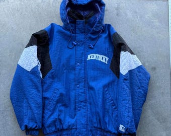 May include: A blue hooded jacket with the word "Kentucky" in white across the chest. The jacket has black and white accents on the sleeves and a quilted pattern. The jacket has a Starter logo on the bottom.