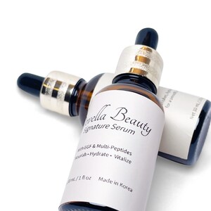 May include: Two brown glass serum bottles with black droppers and gold-colored collars. The bottles have white labels with the text "Vella Beauty Signature Serum" and "with EGF & Multi-Peptides". Each bottle contains 1 fl oz (30 mL) of serum.
