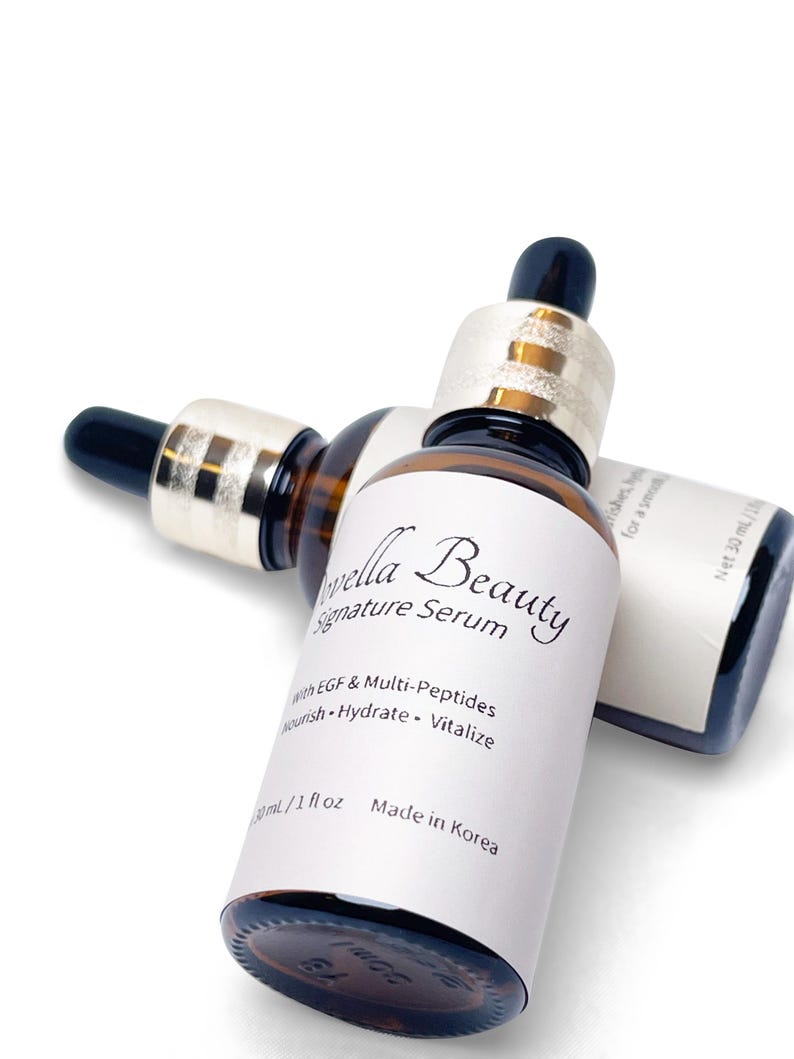 May include: Two brown glass serum bottles with black droppers and gold-colored collars. The bottles have white labels with the text "Vella Beauty Signature Serum" and "with EGF & Multi-Peptides". Each bottle contains 1 fl oz (30 mL) of serum.