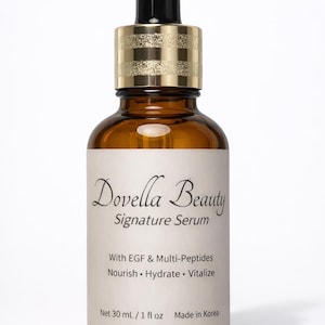 May include: A brown glass bottle of Dovella Beauty Signature Serum with a black dropper and gold-colored cap. The label includes text about the product's ingredients and volume, 1 fl oz.