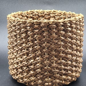 May include: A round, woven basket made of natural materials. The basket is brown and has a natural, rustic look.