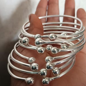 May include: A set of silver bangles with round beads. The bangles are stacked on top of each other and are all the same size.
