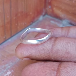 May include: A simple silver band ring with a slightly rounded, oval shape.