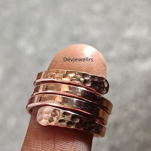 May include: A stack of copper-colored rings with a hammered texture. The rings are wrapped around a finger, showcasing the spiral design. The rings have a warm, metallic sheen, reflecting light.
