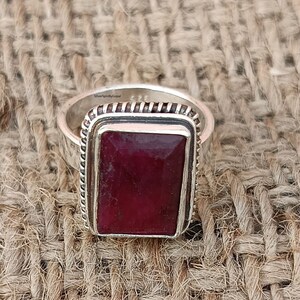May include: A silver ring featuring a rectangular red gemstone set within a silver bezel. The ring has a textured band and is engraved with the text "SilverSpinByGopal".