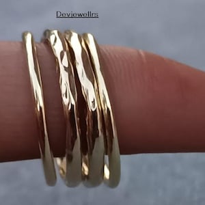 May include: A collection of gold rings, some with a hammered texture, stacked on a finger. The rings vary in design, with some appearing smooth and others displaying a textured surface. The rings are a warm gold color.