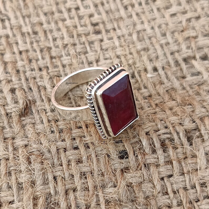 May include: A silver ring with a rectangular red gemstone set in a silver bezel. The ring is on a brown hessian background.