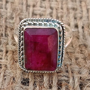 May include: A silver ring with a large, rectangular, deep red ruby gemstone set in a twisted silver band.