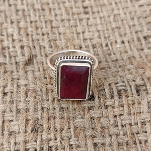 May include: A silver ring featuring a rectangular red ruby gemstone set in a silver bezel. The ring has a textured band.