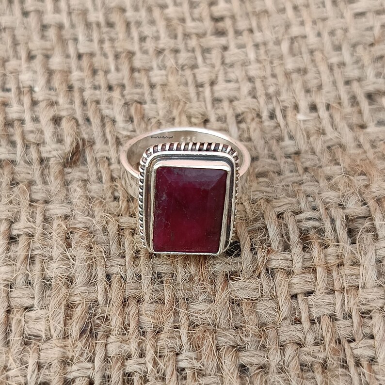 May include: A silver ring featuring a rectangular red ruby gemstone set in a silver bezel. The ring has a textured band.