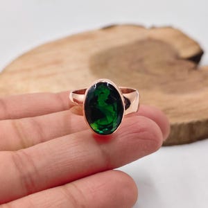 May include: Rose gold ring with a large, oval-cut, deep green gemstone. The ring has a simple, polished band. The setting highlights the vibrant colour of the stone. The gemstone is approximately 2.5 cm in length.
