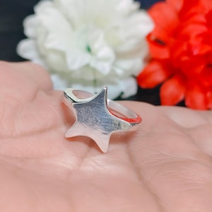 Puede incluir: Un anillo plateado con un diseño en forma de estrella. El anillo tiene un acabado pulido y se encuentra sobre un fondo suave. La estrella tiene cinco puntas y un estilo sencillo y elegante. Una joya.
