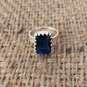 May include: A silver ring with a dark blue rectangular gemstone set in a jagged silver bezel.