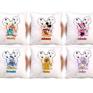 Op de afbeelding: Zes witte sierkussens met Disney-personages: Goofy, Mickey, Minnie, Donald, Pluto en Daisy. Elk kussen heeft een Mickey Mouse-hoofdomtrek met de naam van het personage eronder. De personages zijn in kleur.