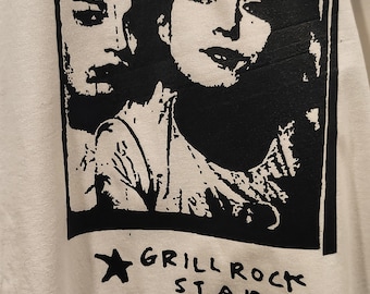 May include: White t-shirt featuring a black and white graphic print. The print includes two faces, the text "Wine. Somethins 1994", and the words "Grill Rock Stars" with a star symbol. The shirt has a crew neck.