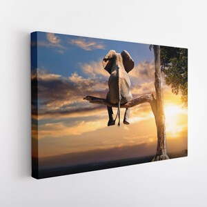 Pode incluir: Um elefante grande está sentado em um galho de uma árvore com um pôr do sol ao fundo. O elefante está de costas para o observador e tem a tromba levantada.