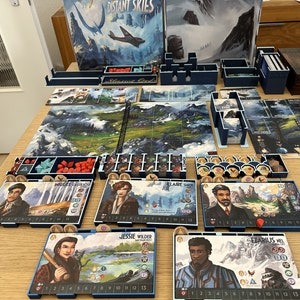 May include: A board game set up for play with a blue and white game board, blue player boards, and wooden tokens. The game board features a mountain range and a river. The game is called "Distant Skies".