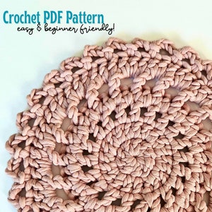 May include: Close-up of a crocheted doily in a pale pink color. The doily has a circular shape and a delicate, lacy design.
