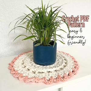May include: A white and pink crochet coaster with a green plant in a blue pot on top. The text "Crochet PDF Pattern easy & beginner friendly!" is written in pink on a white background.