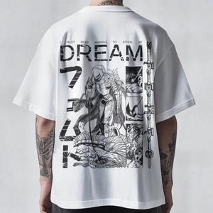 Könnte beinhalten: Weißes T-Shirt mit einer großen Grafik auf der Rückseite, die eine Manga-Illustration eines Kriegers und das Wort "DREAM" zeigt. Das Design enthält japanische Schriftzeichen und den Satz "I must keep winning to attain my".