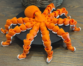 May include: A vibrant orange articulated octopus figurine with white accents on the tentacles. The octopus is posed on a black circular base, with a wooden surface in the background. The figurine is a decorative item.