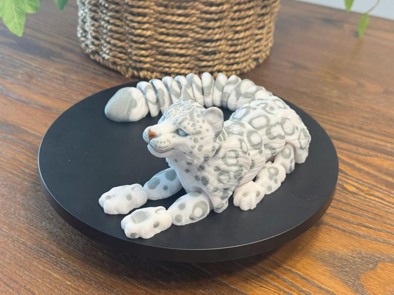 May include: A white and gray snow leopard figurine with a curled tail. The figurine is made of ceramic and has a realistic appearance.