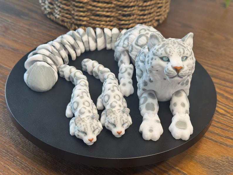 May include: A white snow leopard figurine with a curled tail and two smaller snow leopard figurines. The figurines are made of a white material with gray spots and have realistic details.