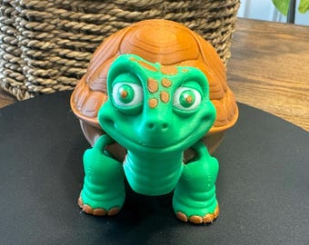 May include: A green and brown turtle figurine with a smiling face and large eyes. The turtle is made of plastic and has a textured shell.