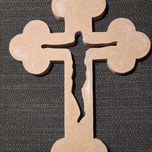 May include: A light brown wooden cross with a distinctive design. The cross has rounded edges and a split vertical beam. This decorative item is likely intended for religious or ornamental use. The cross is made of wood.