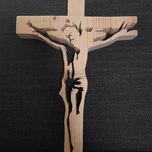 May include: A wooden cross with a cutout design of a person on the cross. The cross is made of light brown wood and has a simple, rustic look.