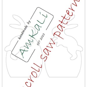 May include: A white paper scroll saw pattern with two bunny designs. The text "scroll saw pattern" is written in red cursive. The AmKali logo is in the center, with the text "handmade by" and "EST 2023".