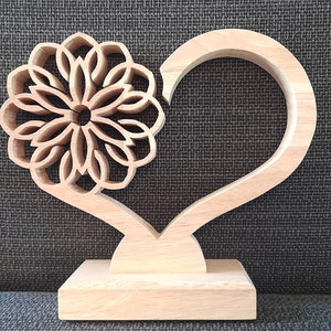 May include: A wooden heart-shaped sculpture with a decorative flower design. The sculpture is made of light brown wood and has a simple, elegant design.
