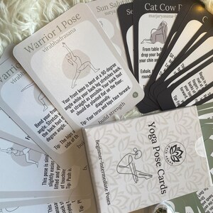 May include: A set of white and black yoga pose cards with illustrations of people in different poses. The cards are labeled with the name of the pose and a tip for performing the pose. The cards are arranged in a pile on a white fuzzy surface.