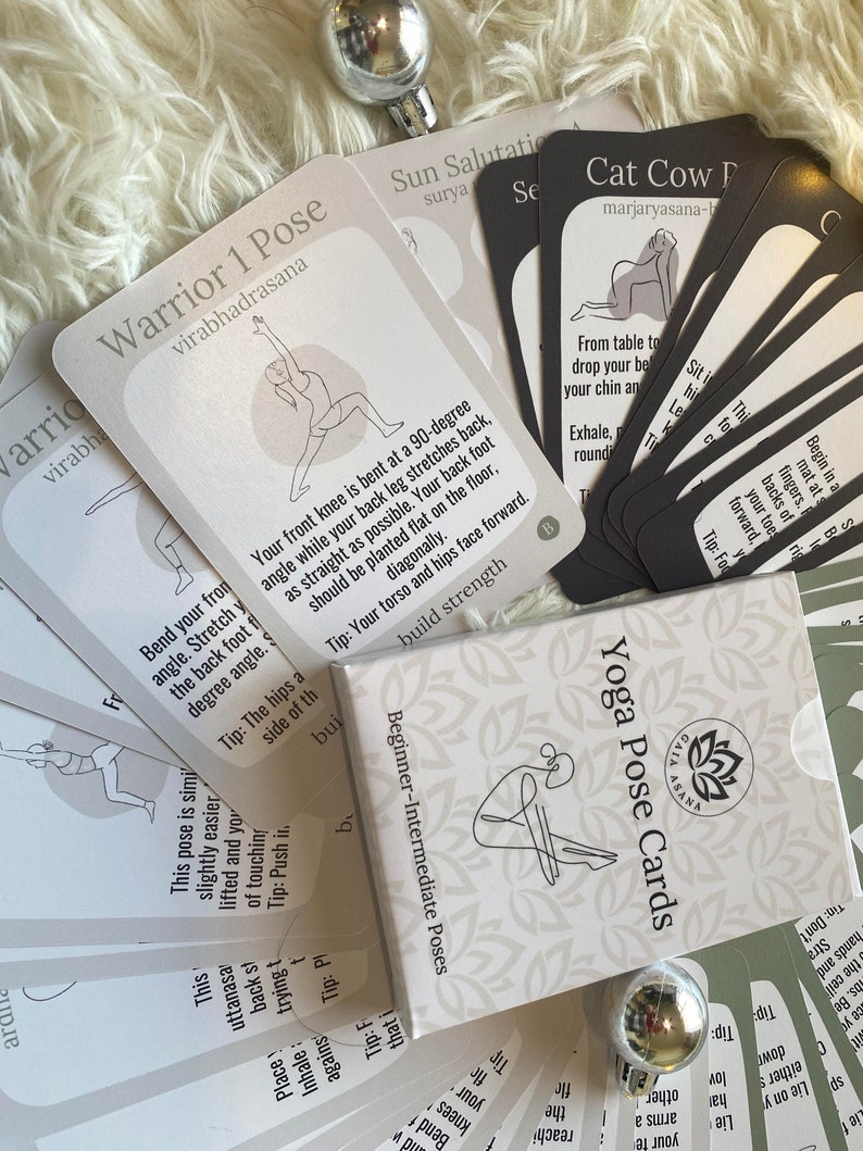 May include: A set of white and black yoga pose cards with illustrations of people in different poses. The cards are labeled with the name of the pose and a tip for performing the pose. The cards are arranged in a pile on a white fuzzy surface.