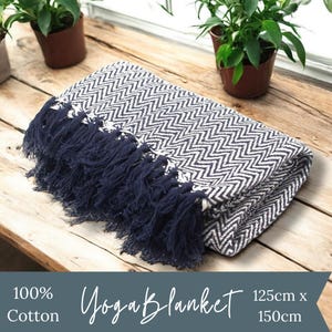 May include: A navy blue and white chevron patterned yoga blanket with navy blue fringe. The blanket is made of 100% cotton and measures 125cm x 150cm. Yoga Blanket.