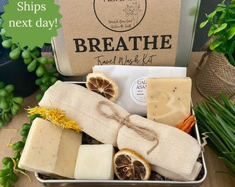May include: A metal tin with a brown label that reads "GAIA ASANA" and "BREATHE Travel Wash Kit". The tin contains a white washcloth, four bars of soap, and dried lemon slices. The label also says "Vegan * Eco * Natural".
