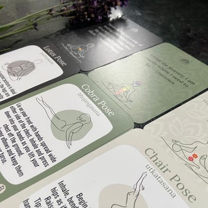May include: A set of green and black yoga pose cards with illustrations and text. The cards feature poses like Lotus Pose, Cobra Pose, and Chair Pose. The text includes quotes about yoga and the journey of life.