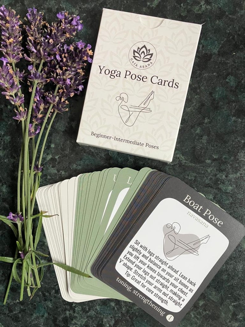 May include: A deck of yoga pose cards with a green and black design. The card shown features a line drawing of a person in the boat pose, with the name of the pose, "Boat Pose", and the Sanskrit name, "navasana", printed in black text. The card also includes instructions for the pose and a description of its benefits, "toning, strengthening".