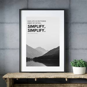 Puede incluir: Una impresión enmarcada en blanco y negro con una cita de Henry David Thoreau: "Nuestra vida se desperdicia en los detalles. Simplifica, simplifica." La cita está centrada en un fondo blanco. La imagen debajo de la cita es una fotografía en blanco y negro de un lago y montañas.