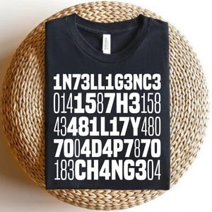 Puede incluir: Camiseta negra con texto blanco: 1N73LL1G3NC3, 0141587H3158, 43481L17Y480, 7004D4P7870, 183CH4NG304. La camiseta está sobre una superficie redonda, tejida, de color marrón claro.