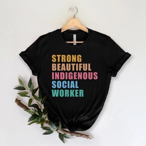 May include: Black t-shirt with the words "STRONG", "BEAUTIFUL", "INDIGENOUS", "SOCIAL", and "WORKER" printed in rainbow colors.