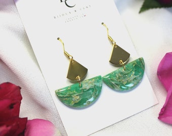 May include: A pair of green and gold earrings with a geometric design. The earrings are made of polymer clay and have a marbled effect. The earrings are hanging from gold hooks.