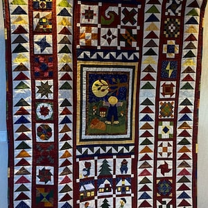 May include: A colourful quilt with a patchwork design featuring a variety of geometric shapes and patterns. The quilt includes a central panel depicting a scarecrow in a field with a full moon. The quilt is made with a variety of fabrics in shades of red, blue, green, yellow, and white.