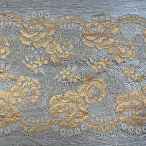 May include: Gold and ivory lace trim with a floral pattern. The lace has a delicate, intricate design with small flowers and leaves.