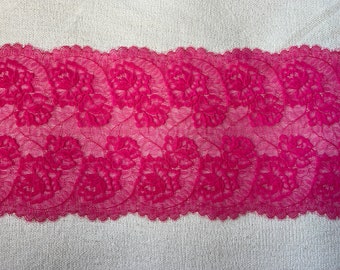 May include: Pink lace trim with a floral pattern. The lace is delicate and has a scalloped edge.