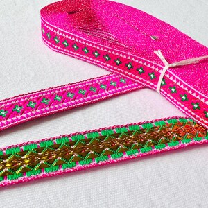 May include: Two pink and green trim ribbons with gold accents. The ribbon on top has a white background with a repeating diamond pattern. The ribbon on the bottom has a green and gold chevron pattern.